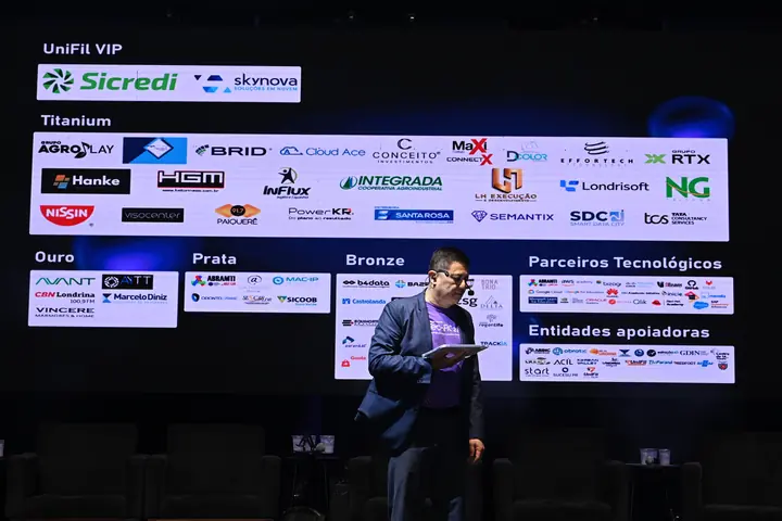 Apresentador diante do telão com as marcas dos patrocinadores da TechFil 2026
